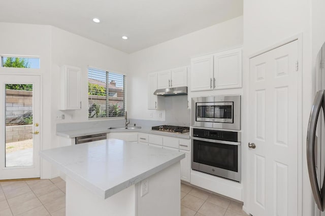 kitchen with appliances with stainless steel finishes, a kitchen island, white cabinetry, sink, and light tile patterned flooring