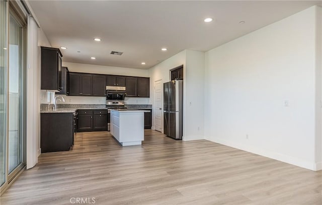 kitchen with dark brown cabinetry, appliances with stainless steel finishes, light hardwood / wood-style floors, and a kitchen island