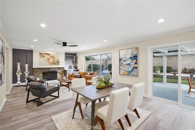 dining space with light hardwood / wood-style floors, ornamental molding, and a stone fireplace