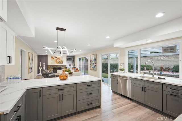 kitchen with stainless steel dishwasher, sink, a stone fireplace, and gray cabinets