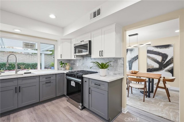 kitchen with gray cabinets, sink, light hardwood / wood-style flooring, white cabinets, and gas range