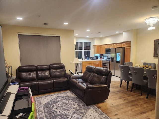 living room with sink, a notable chandelier, and light hardwood / wood-style floors