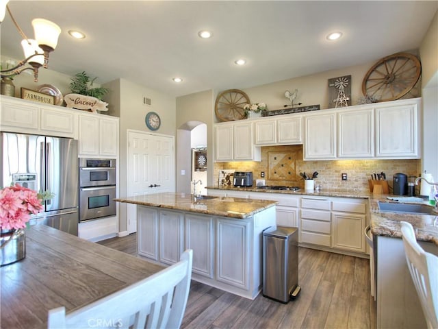 kitchen with stainless steel appliances, backsplash, a kitchen island with sink, light stone countertops, and sink