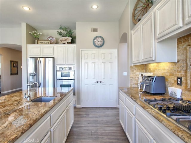 kitchen with white cabinets, stainless steel appliances, tasteful backsplash, sink, and light stone counters