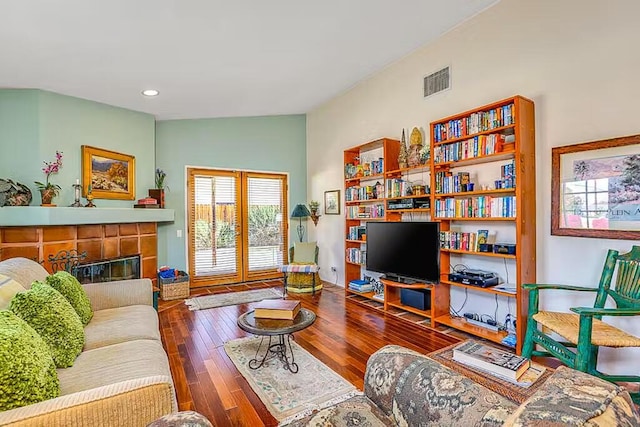 living room featuring a tiled fireplace, dark wood-type flooring, and vaulted ceiling