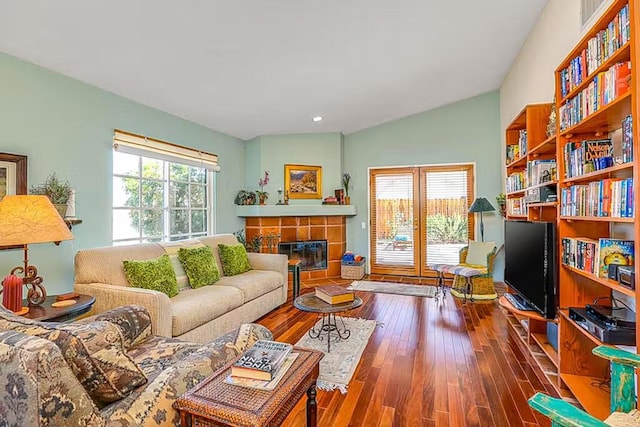 living room featuring dark hardwood / wood-style floors, a tiled fireplace, and vaulted ceiling