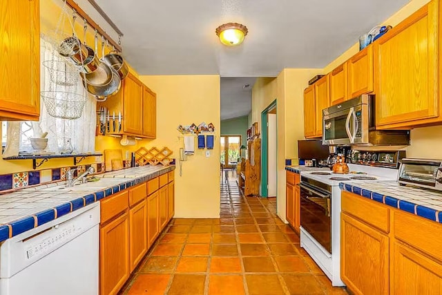 kitchen with light tile patterned floors, tile counters, sink, and white appliances