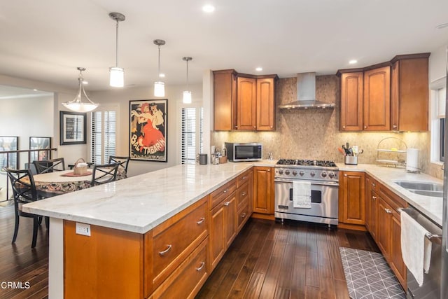 kitchen featuring kitchen peninsula, appliances with stainless steel finishes, wall chimney exhaust hood, and hanging light fixtures