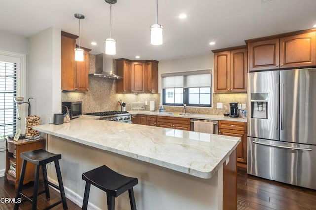 kitchen with light stone countertops, appliances with stainless steel finishes, wall chimney range hood, sink, and kitchen peninsula