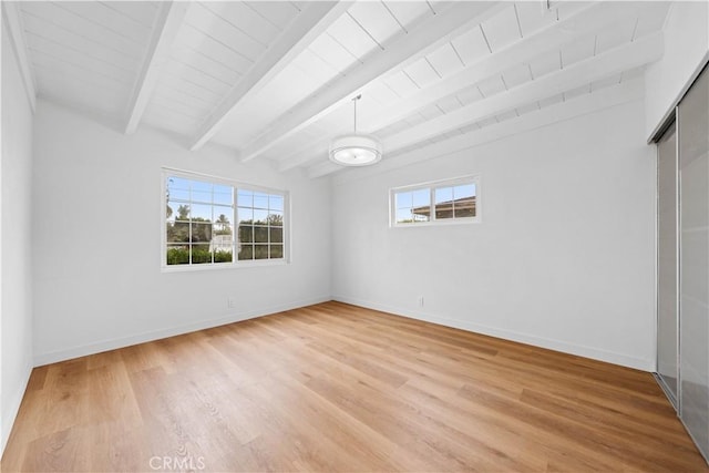 spare room with beamed ceiling and light wood-type flooring