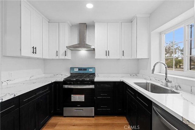 kitchen featuring wall chimney range hood, sink, appliances with stainless steel finishes, white cabinets, and light stone counters