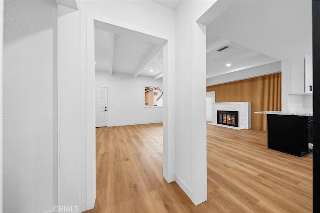 hallway with beamed ceiling, wooden walls, and light hardwood / wood-style flooring