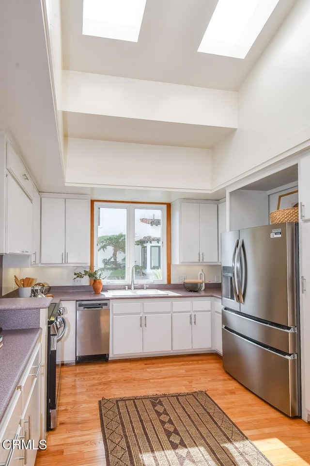 kitchen featuring light hardwood / wood-style floors, sink, white cabinetry, a skylight, and appliances with stainless steel finishes