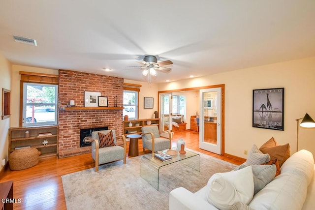 living room with light wood-type flooring, ceiling fan, and a brick fireplace