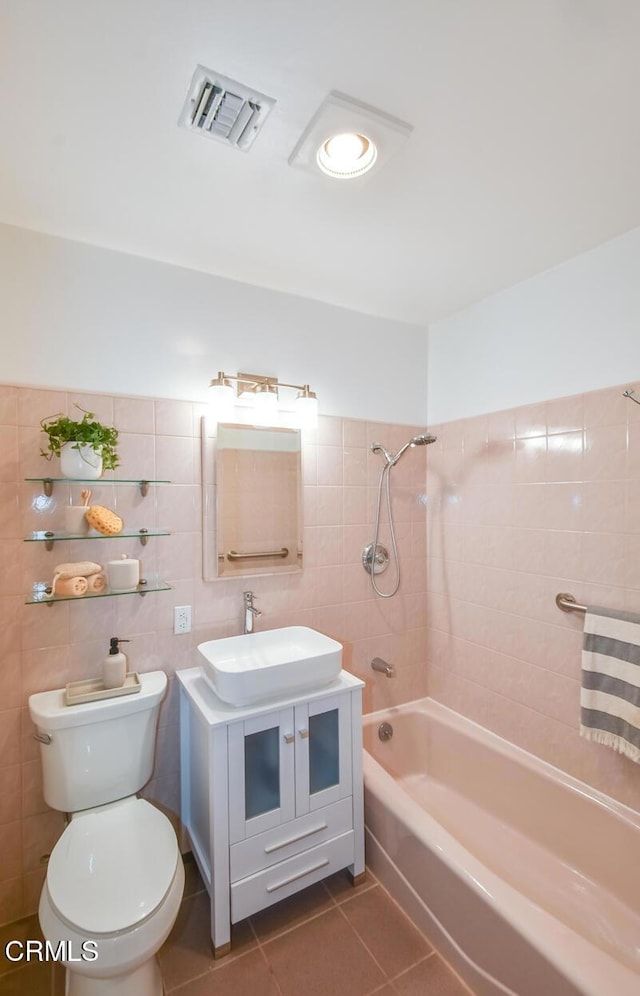 full bathroom featuring tiled shower / bath combo, tile patterned floors, vanity, tile walls, and toilet