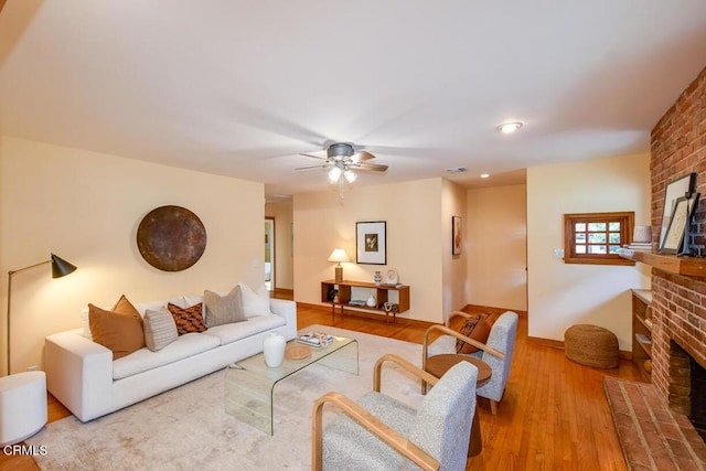 living room with a fireplace, ceiling fan, and light wood-type flooring