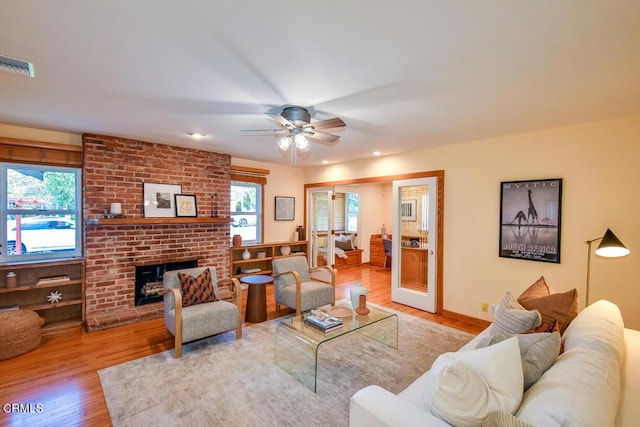 living room featuring light wood-type flooring, ceiling fan, a wealth of natural light, and a fireplace