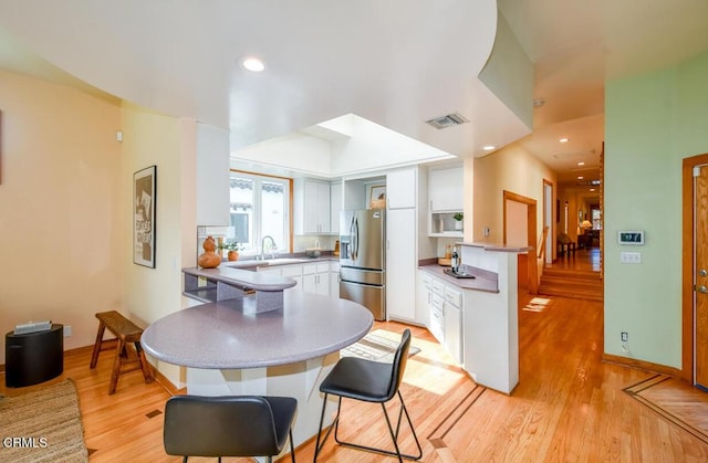 kitchen with a breakfast bar, kitchen peninsula, white cabinetry, light hardwood / wood-style flooring, and stainless steel fridge