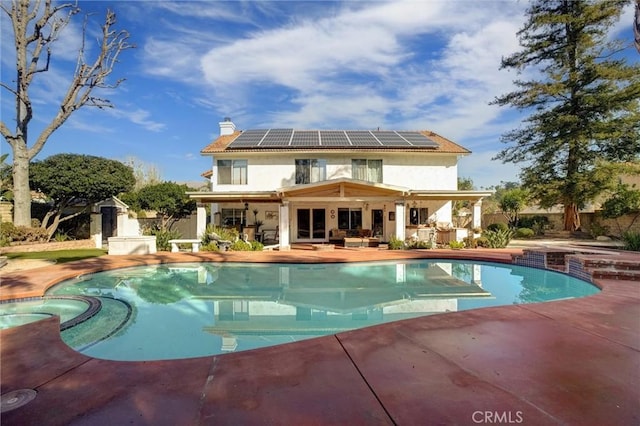 rear view of property with a swimming pool with hot tub, solar panels, and a patio