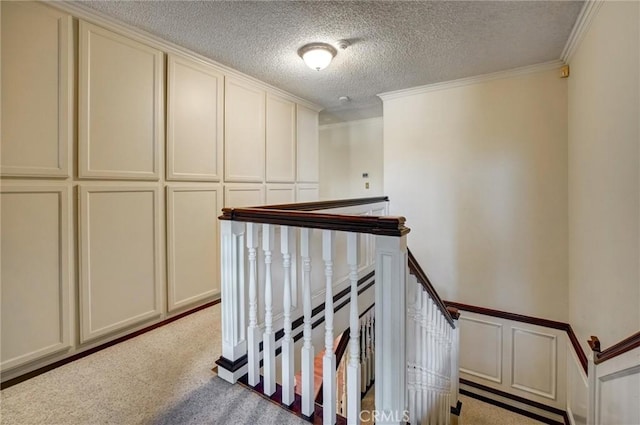 hall with light colored carpet, a textured ceiling, and ornamental molding