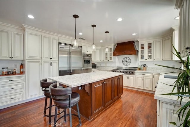 kitchen with a kitchen island, a breakfast bar, stainless steel appliances, custom range hood, and white cabinets