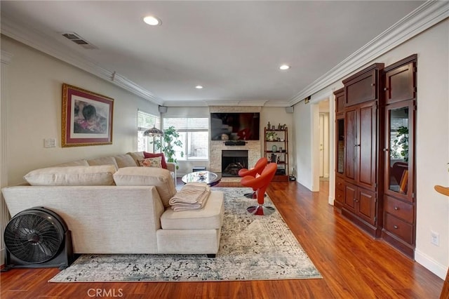 living room with a stone fireplace, ornamental molding, and hardwood / wood-style floors