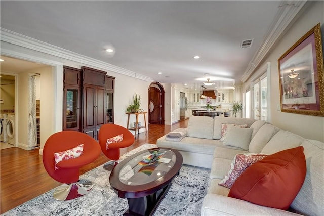 living room featuring washing machine and dryer, ornamental molding, and wood-type flooring