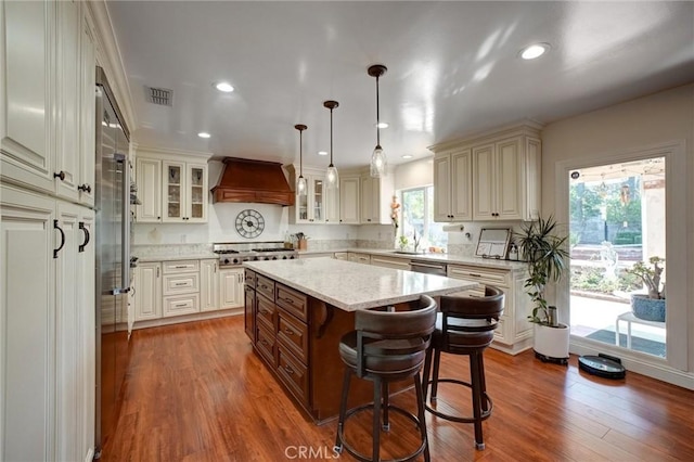 kitchen with decorative light fixtures, a kitchen island, a kitchen breakfast bar, custom range hood, and dark hardwood / wood-style flooring