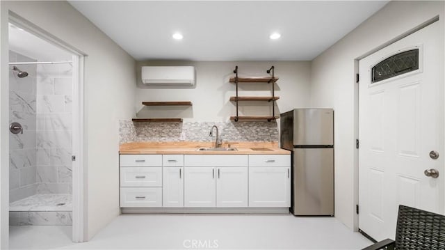 kitchen with an AC wall unit, sink, stainless steel refrigerator, white cabinetry, and wood counters