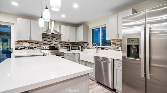 kitchen featuring appliances with stainless steel finishes, decorative light fixtures, wall chimney range hood, white cabinetry, and sink