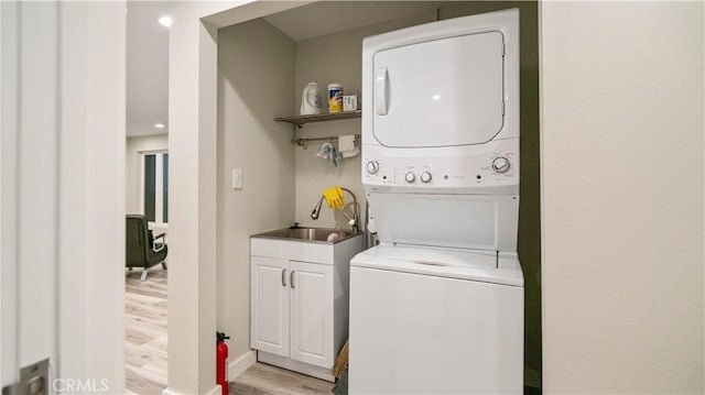 clothes washing area featuring stacked washer / drying machine, light wood-type flooring, and sink