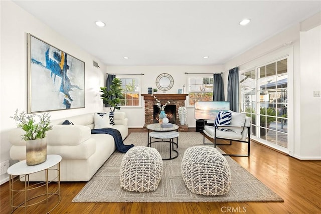 living room with a brick fireplace, a wealth of natural light, and hardwood / wood-style flooring