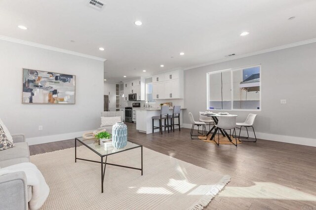 living area with visible vents, wood finished floors, and ornamental molding