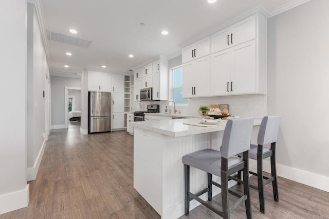 kitchen featuring visible vents, a peninsula, a sink, stainless steel appliances, and tasteful backsplash