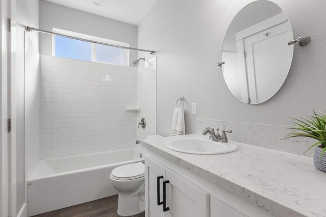 full bath with toilet, wood finished floors,  shower combination, vanity, and a textured wall