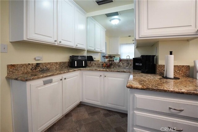 kitchen featuring white cabinetry, stone counters, stone finish floor, and visible vents