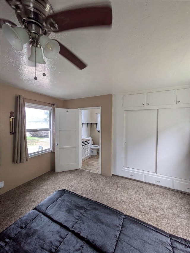 unfurnished bedroom featuring light carpet, ceiling fan, ensuite bath, and a textured ceiling