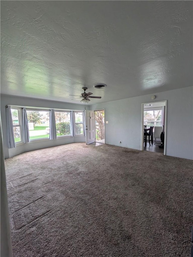 unfurnished living room featuring a ceiling fan, a wealth of natural light, carpet, and visible vents
