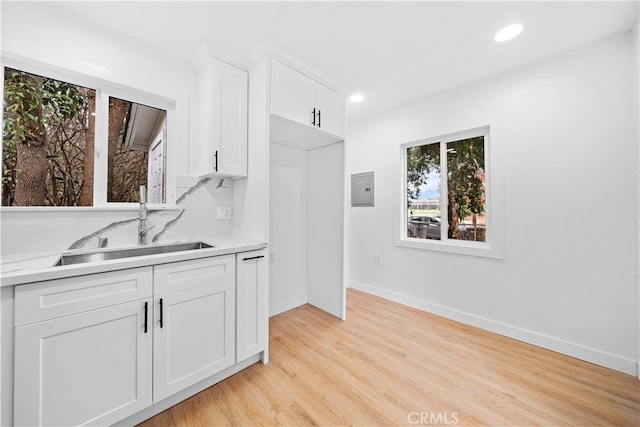 kitchen with backsplash, white cabinets, light stone countertops, light hardwood / wood-style flooring, and sink