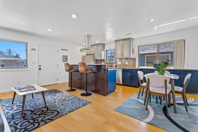 interior space featuring decorative backsplash, a healthy amount of sunlight, light wood-type flooring, blue cabinetry, and a breakfast bar area