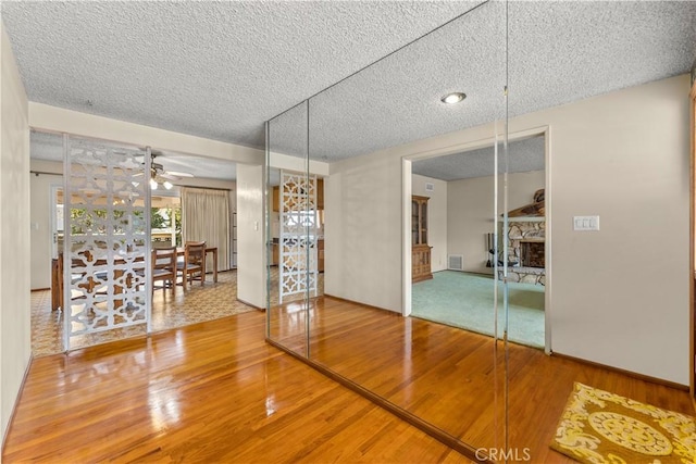 interior space with a textured ceiling, ceiling fan, a fireplace, and wood-type flooring