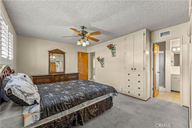 bedroom with ceiling fan, light colored carpet, a textured ceiling, and ensuite bathroom