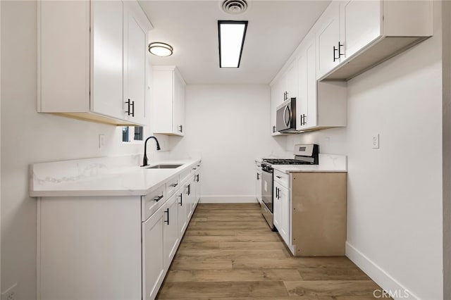 kitchen with stainless steel appliances, light hardwood / wood-style floors, white cabinetry, and sink