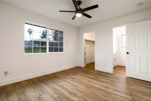 unfurnished bedroom featuring ceiling fan, a walk in closet, a closet, and light hardwood / wood-style flooring