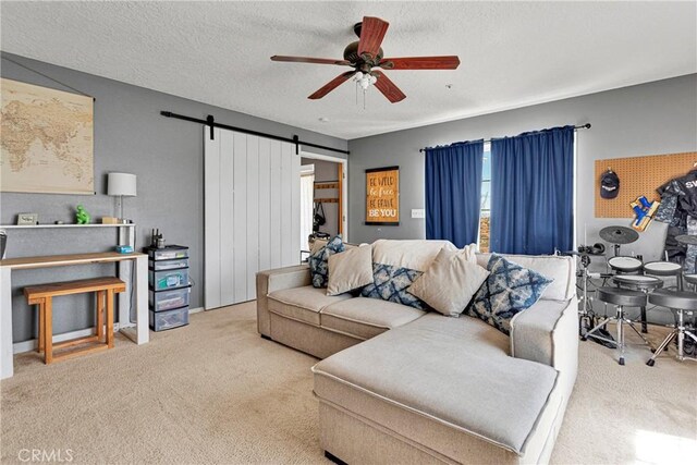 living room with ceiling fan, a barn door, carpet floors, and a textured ceiling