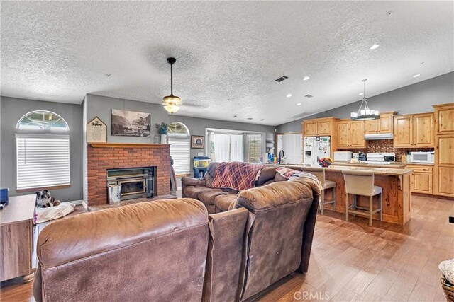 living room with a brick fireplace, a textured ceiling, and vaulted ceiling