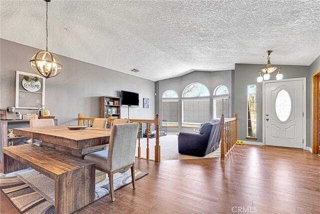 dining room featuring a textured ceiling, a chandelier, lofted ceiling, and hardwood / wood-style floors