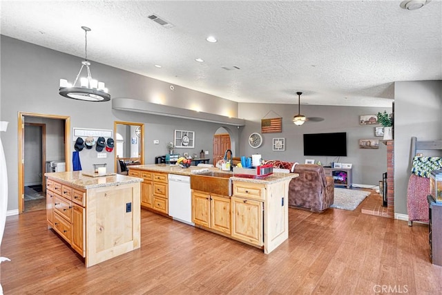 kitchen featuring light brown cabinetry, white dishwasher, hanging light fixtures, and a kitchen island with sink