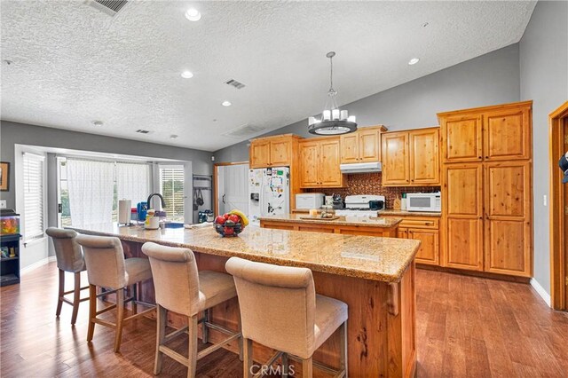 kitchen with a large island, decorative backsplash, decorative light fixtures, white appliances, and lofted ceiling