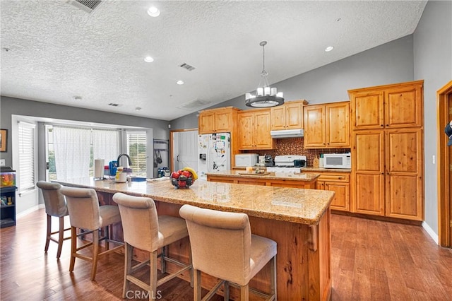 10187 Mesquite St, Oak Hills, CA 92344 - kitchen with a large island with sink, white appliances, a textured ceiling, lofted ceiling, and under cabinet range hood